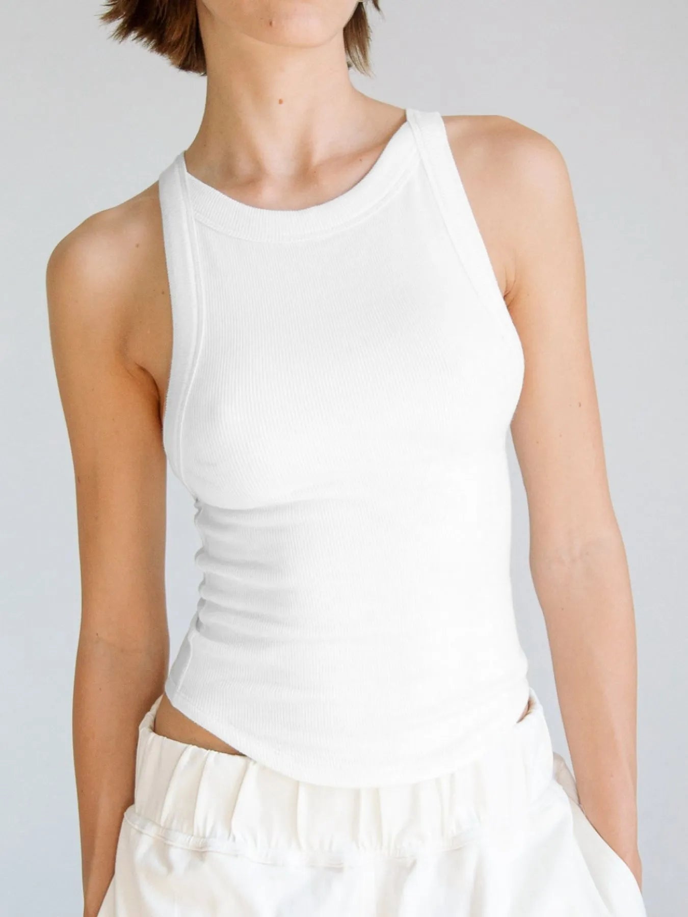 White asymmetrical back ribbed crop tank top for women, designed with a fitted silhouette and ribbed texture, ideal for casual wear or layering in warmer weather