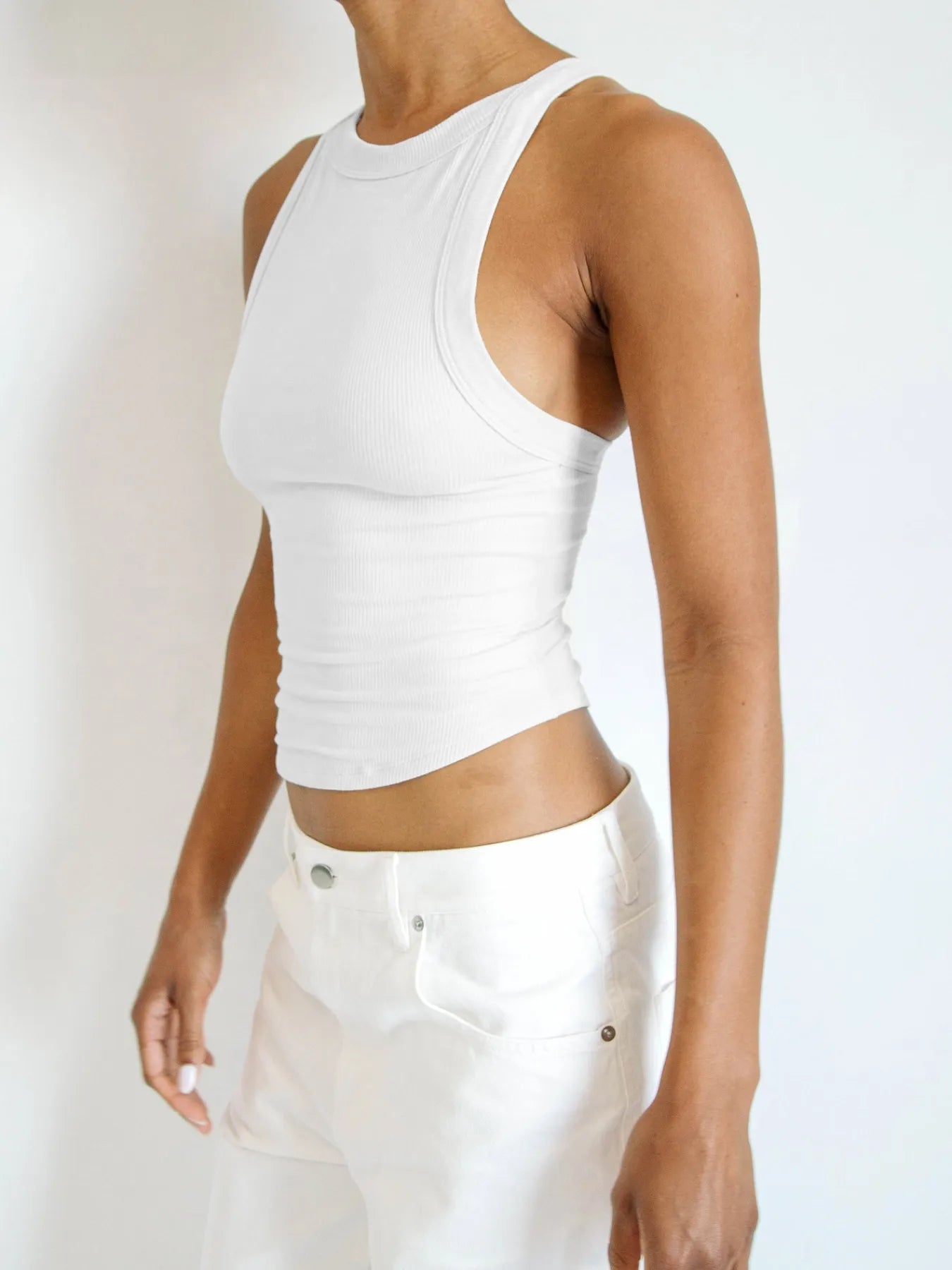 White asymmetrical back ribbed crop tank top for women, designed with a fitted silhouette and ribbed texture, perfect for casual wear or layering in warm weather