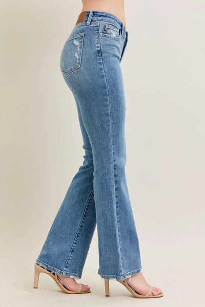 Angled front view of Judy Blue Full Size Mid Rise Wash Destroy Hem Bootcut Jeans Plus Size, showcasing the silhouette.